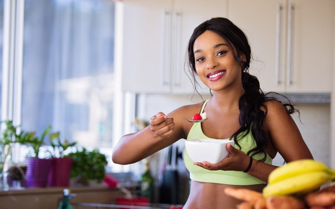 sporty woman in kitchen eating a bowl of fruit