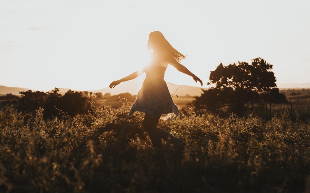 woman spinning around in field with sunlight behind her
