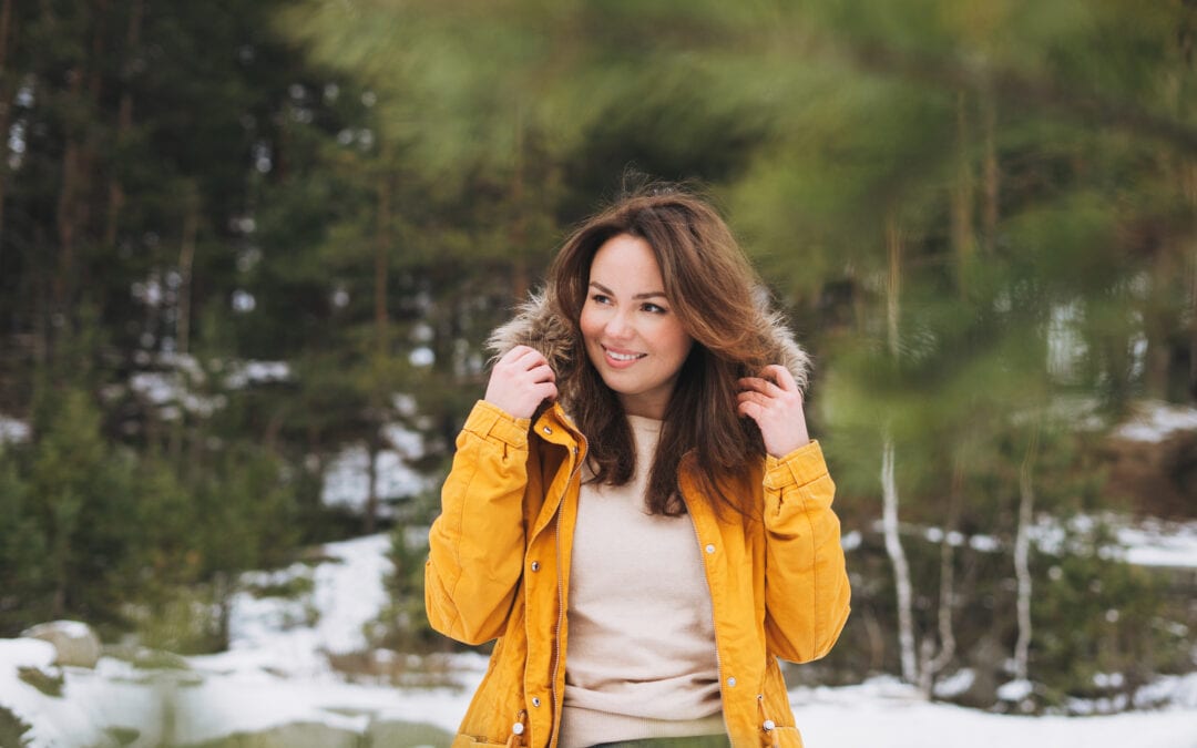 Woman outside in a coat in front of a snowy forest setting