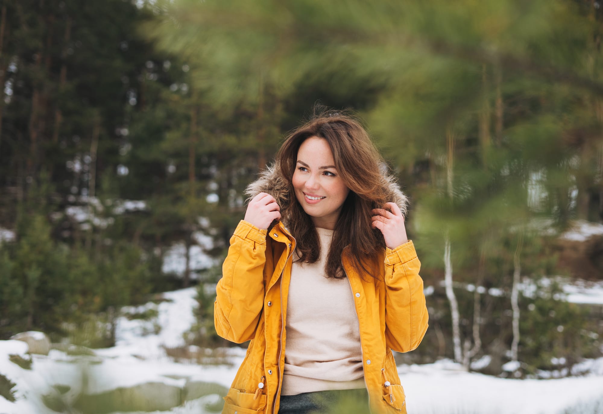 Woman outside in a coat in front of a snowy forest setting