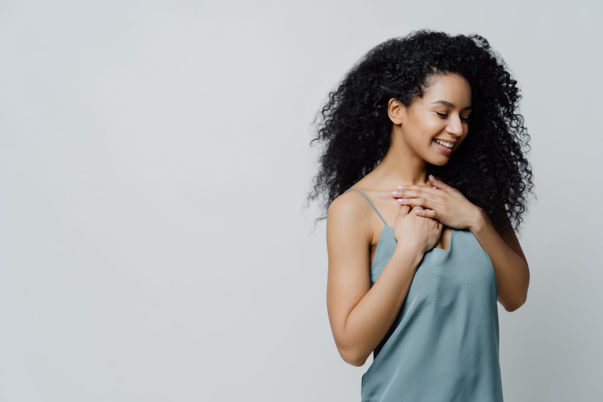 Profile Of Dreamy Romantic Ethnic Woman With Afro Haircut, Dressed In Nightwear, Keeps Hands On Chest, Recalls Very Pleasant Moment In Life Smiles Tenderly With Closes Eyes Expresses Truthful Feelings