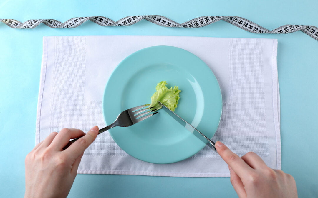 Picture of female hands holding knife and fork on plate cutting piece of lettuce leaf, top view