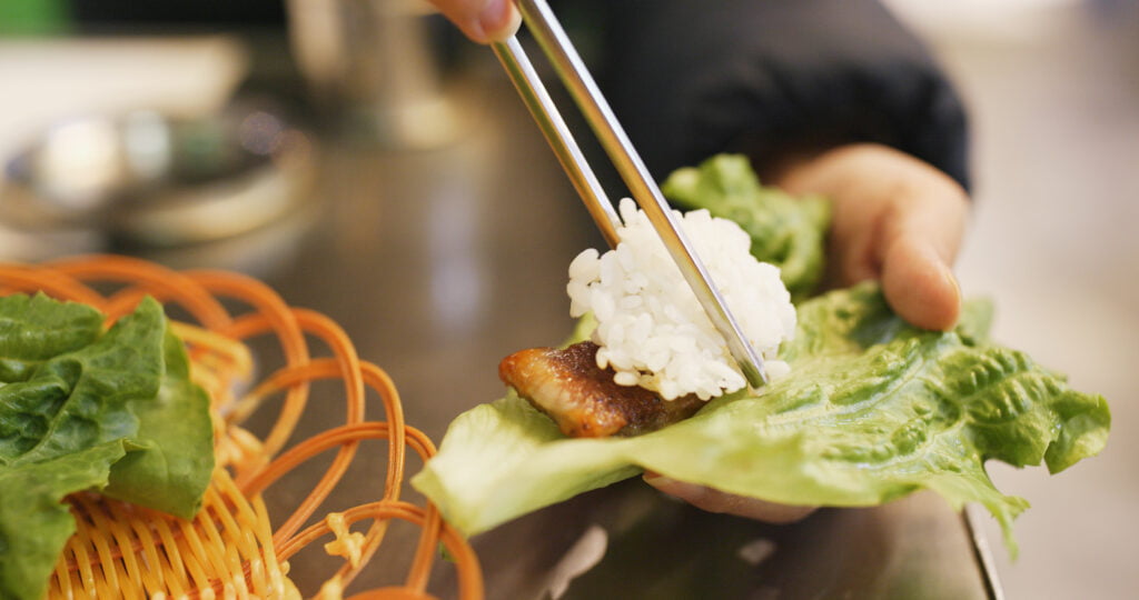 woman wrapping grilled korean meat in lettuce at restaurant