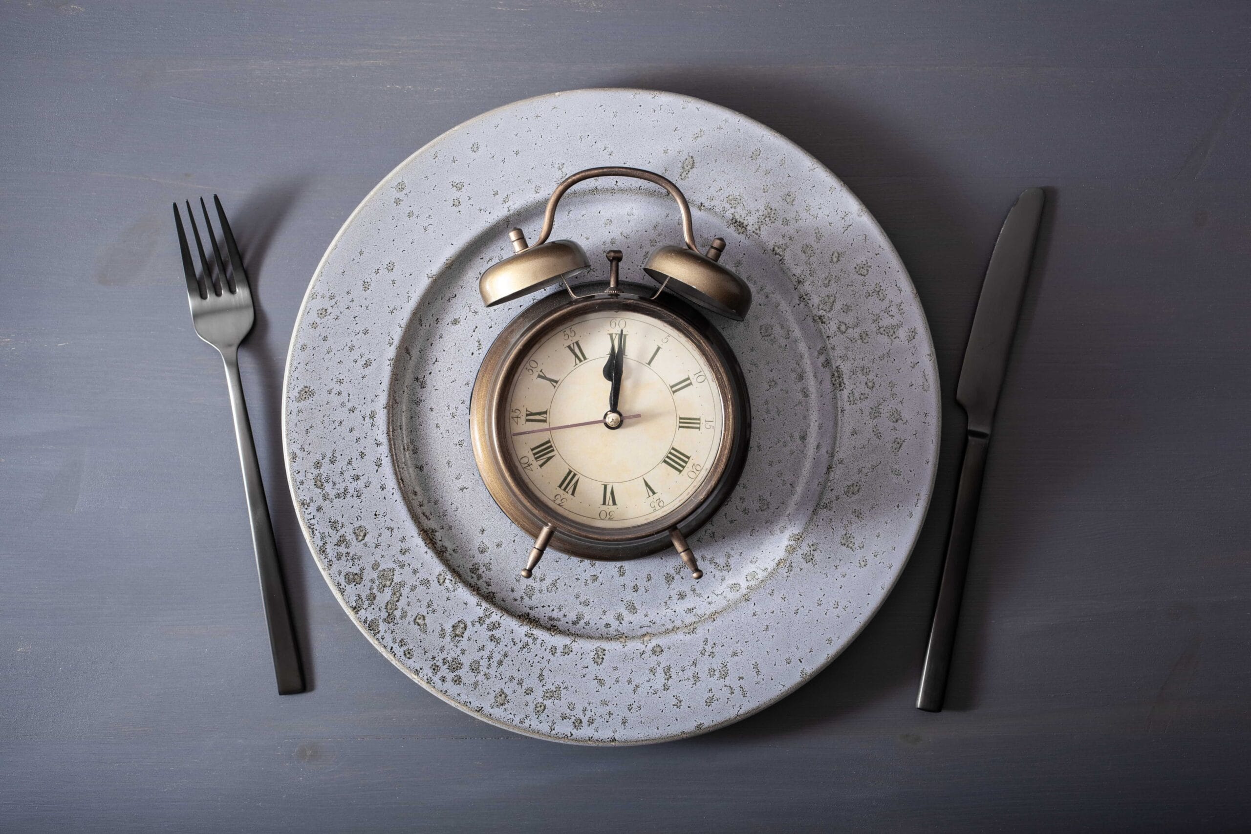 Alarm clock sitting on a speckled plate between a fork and a knife