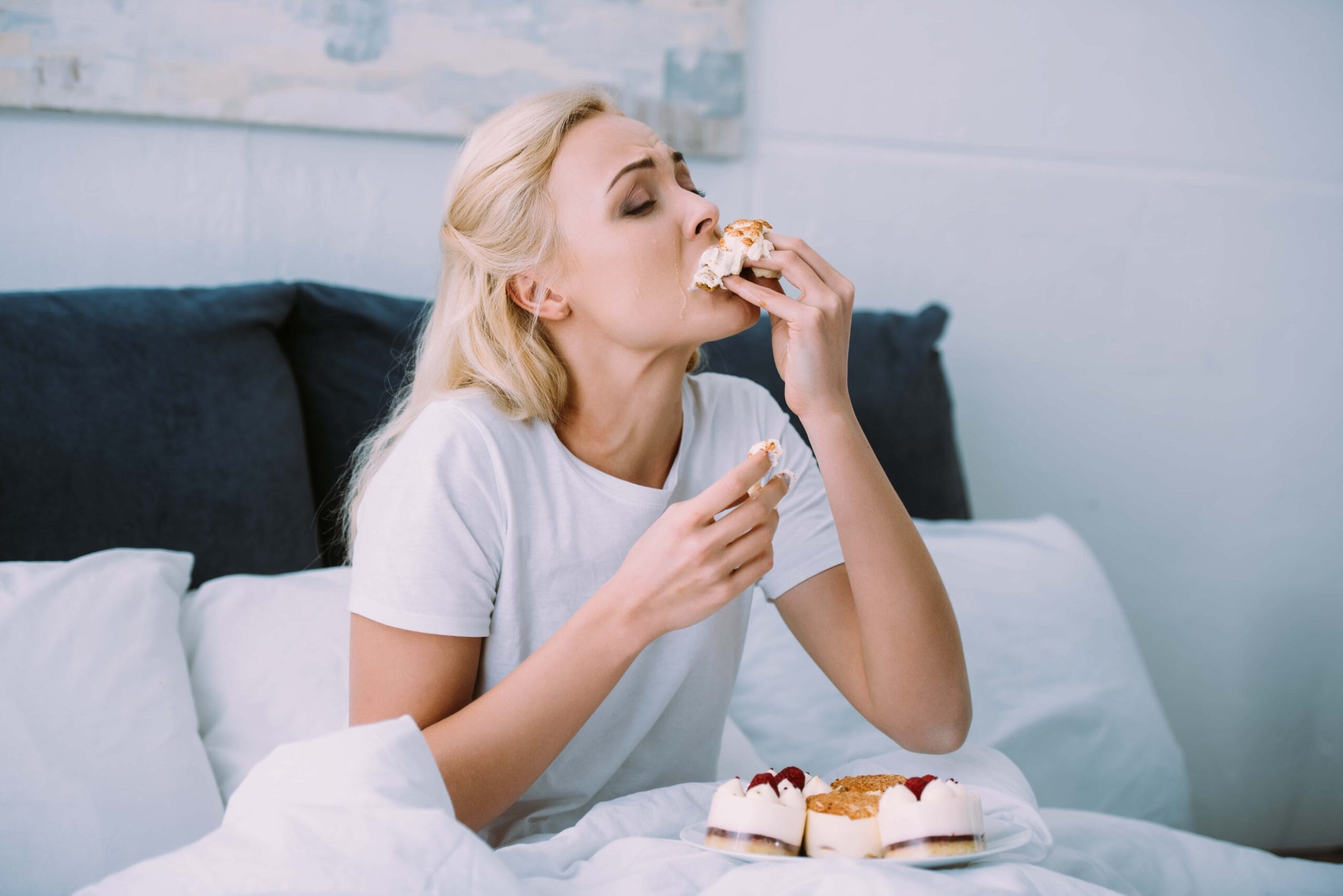 Woman sitting up in bed eating strawberry cheesecake with her bare hands