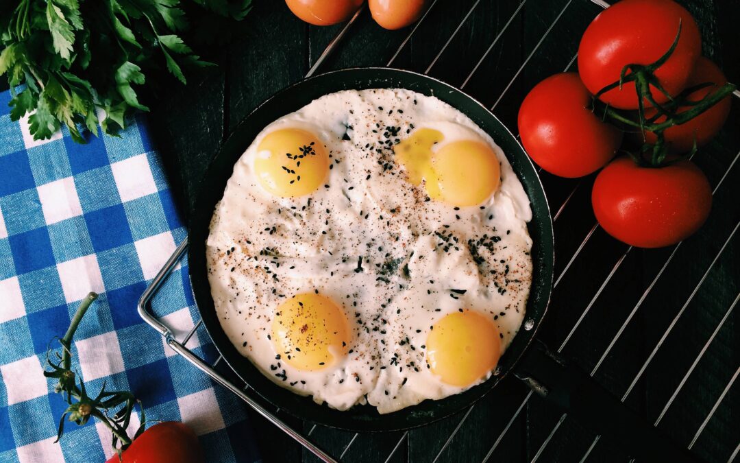 Four sunny side up eggs on a cast iron skillet surrounded by fresh veggies on a cooling rack