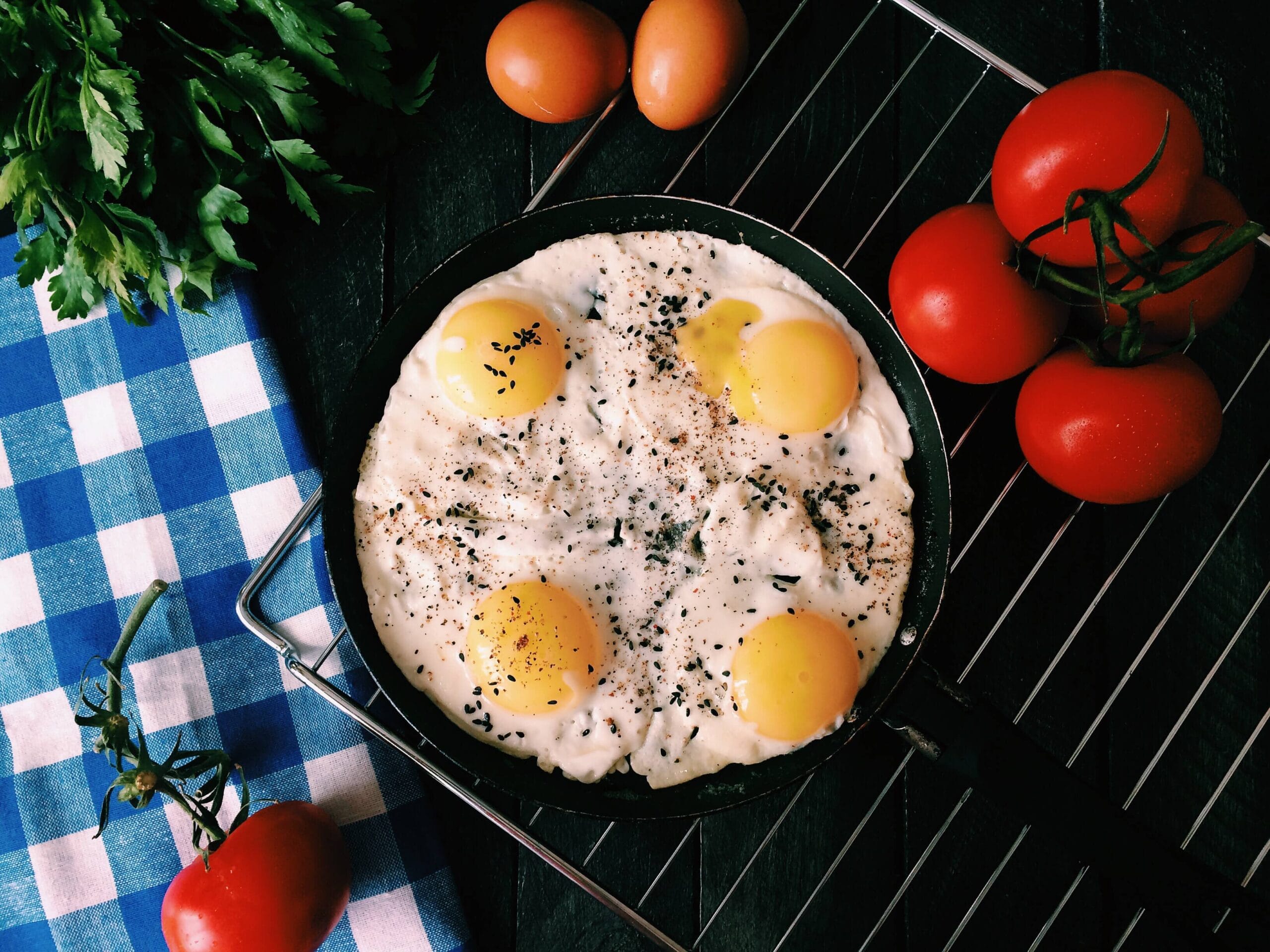 Four sunny side up eggs on a cast iron skillet surrounded by fresh veggies on a cooling rack