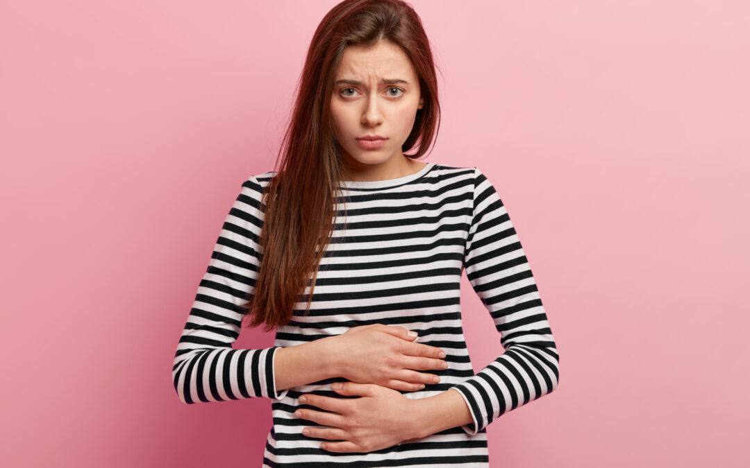 frowning woman holding her gut infront of pink wall