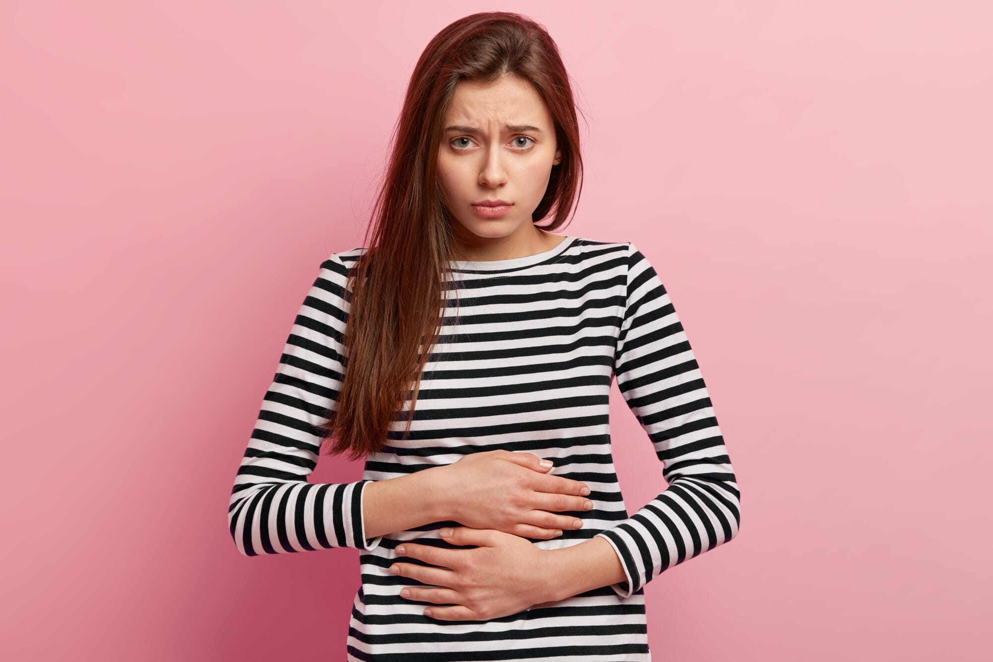 frowning woman holding her gut infront of pink wall