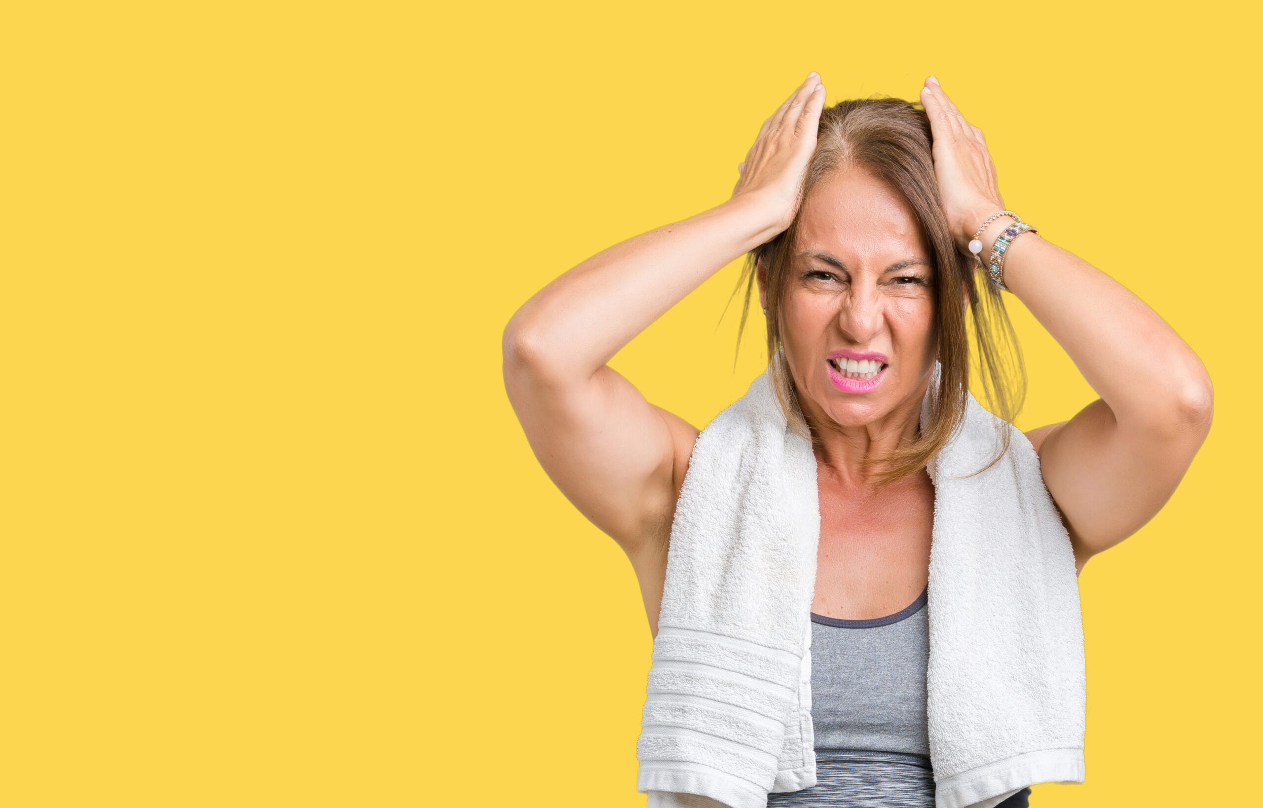 beautiful middle age woman wearing sport clothes and a towel over isolated background suffering from headache desperate and stressed because pain and migraine. hands on head.