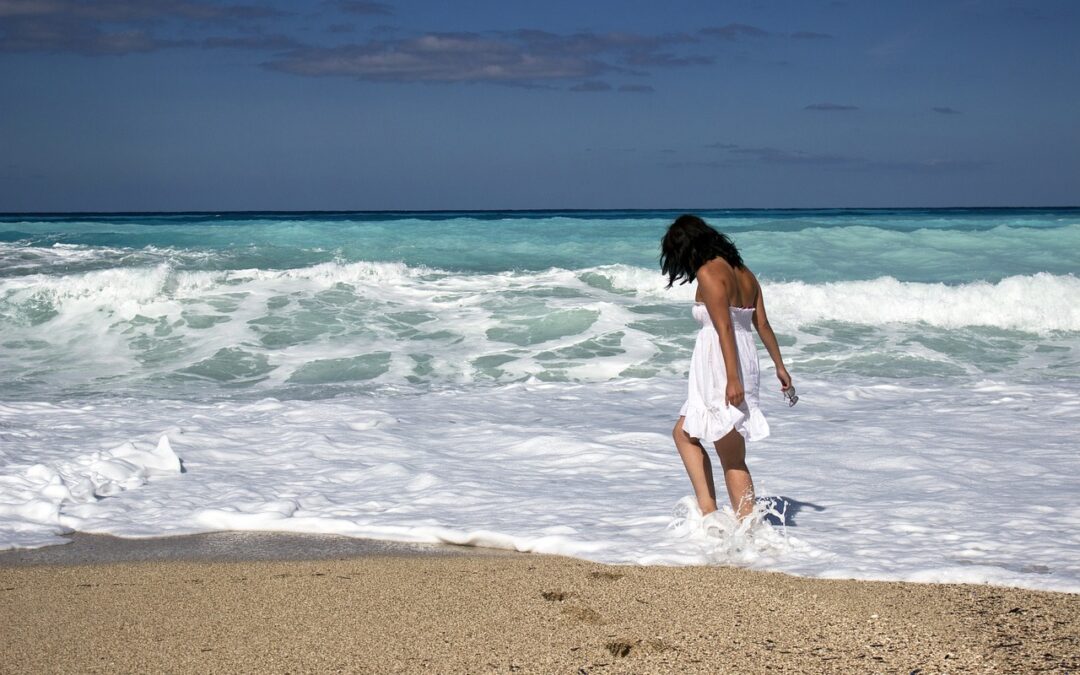 woman in white sundress walking in surf at beach on sunny day