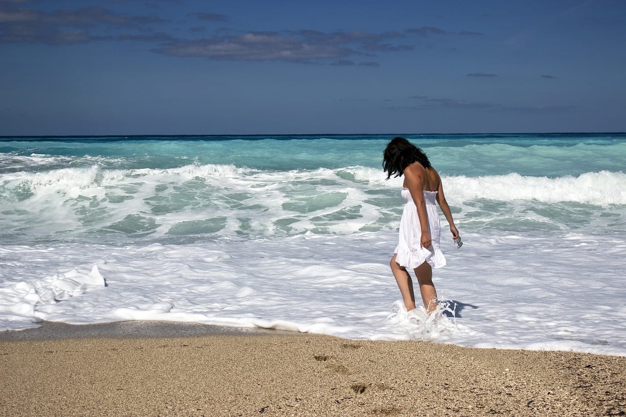 woman in white sundress walking in surf at beach on sunny day