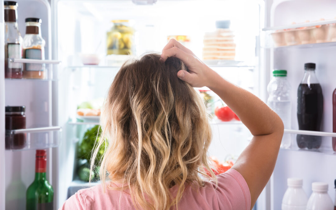 confused woman looking in open refrigerator