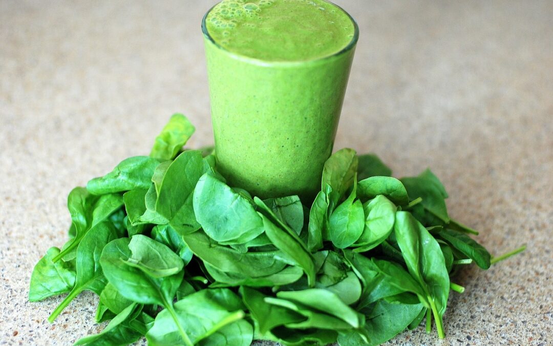 green_smoothie_with_spinach_leaves_around_base_of_glass_on_table