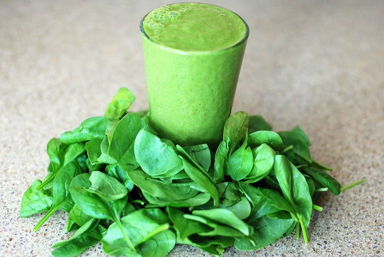 green_smoothie_with_spinach_leaves_around_base_of_glass_on_table
