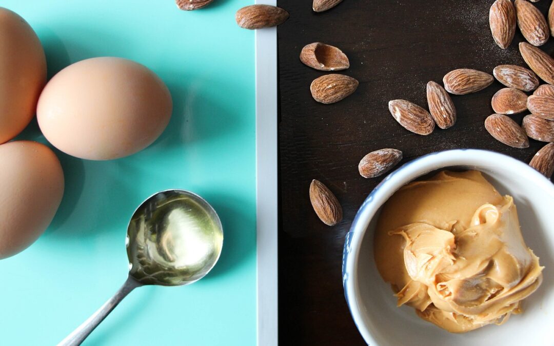 healthy_fat_foods_eggs_peanut_butter_almonds_olive_oil_on_table