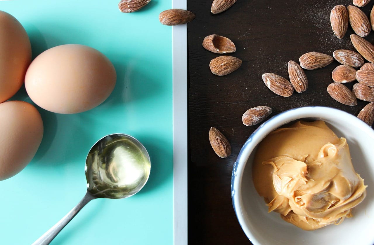 healthy_fat_foods_eggs_peanut_butter_almonds_olive_oil_on_table