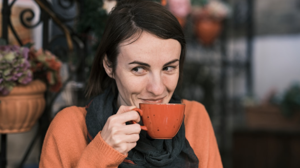woman_in_orange_shirt_sipping_coffee_and_smirking