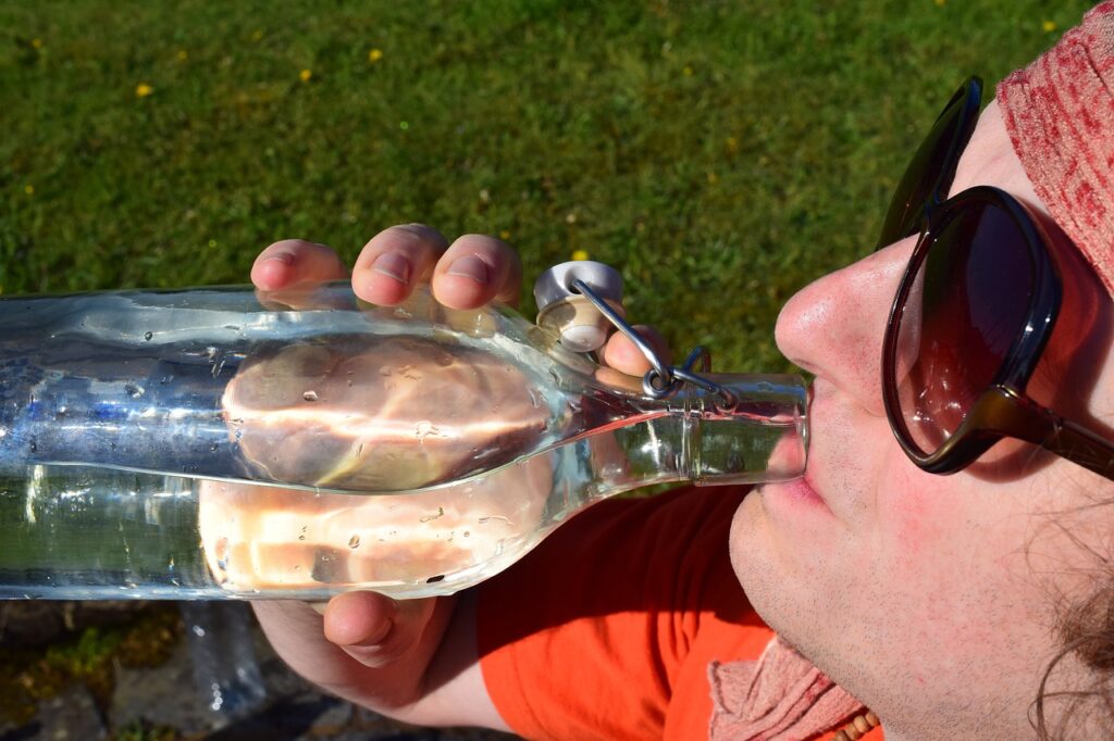 close_up_of_man_drinking_water_out_of_glass_bottle_hot_summer_day