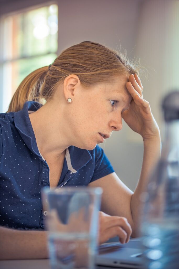 stressed woman leaning on hand infront of computer with glass of water