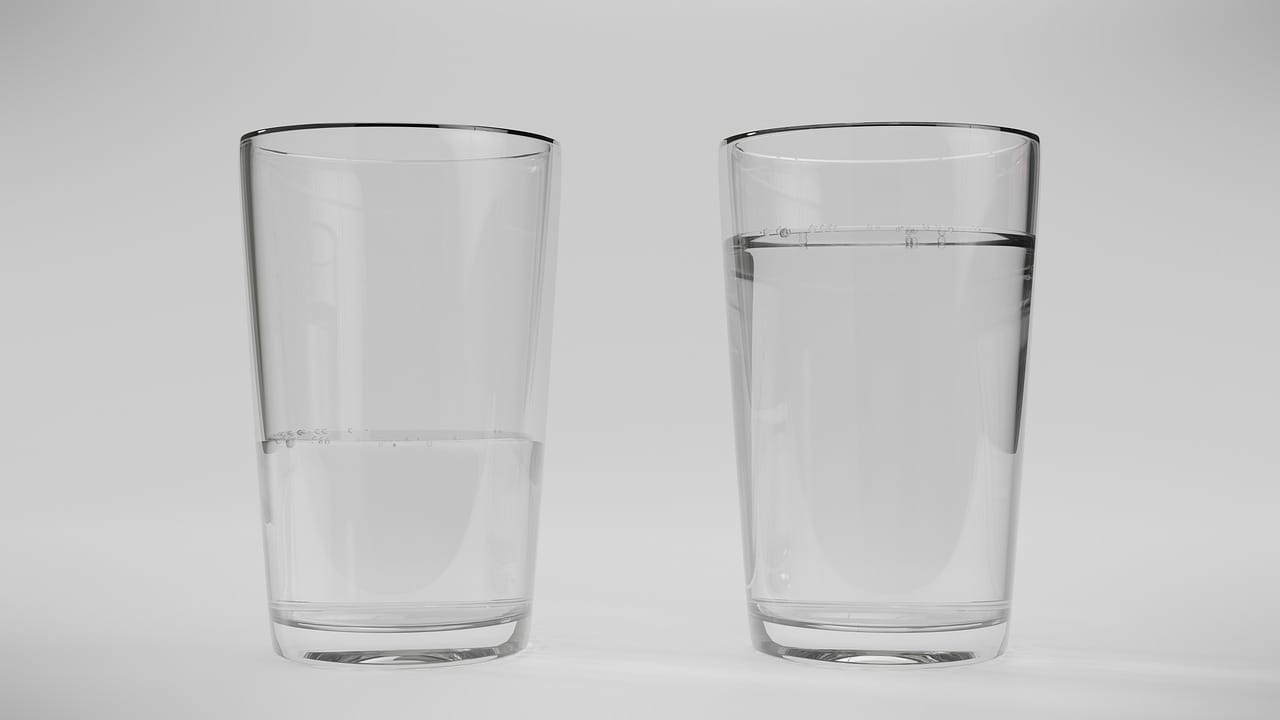 two water glasses one full and one half empty on a white background