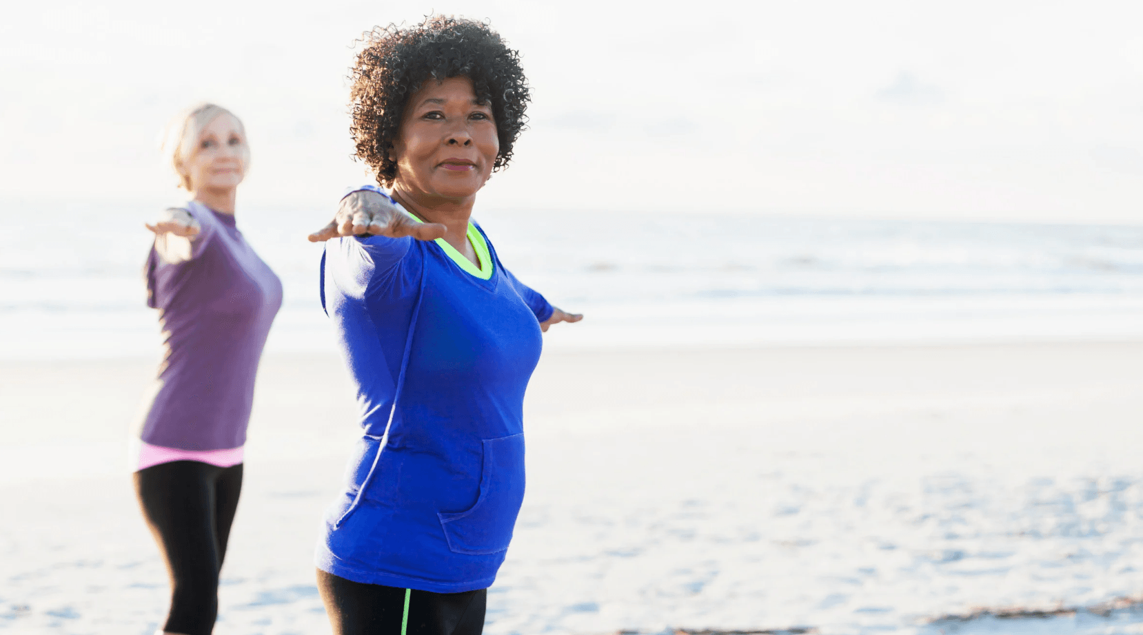 two older women over 50 doing yoga on the beach