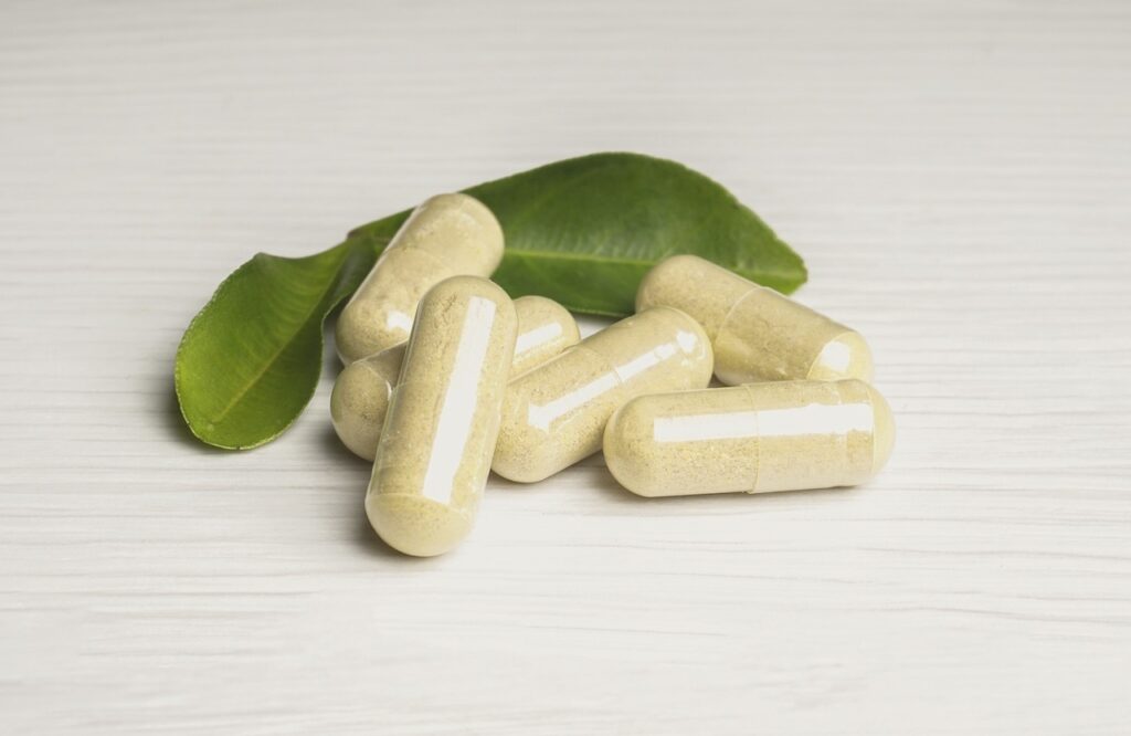 pill capsules with leaves sitting behind them