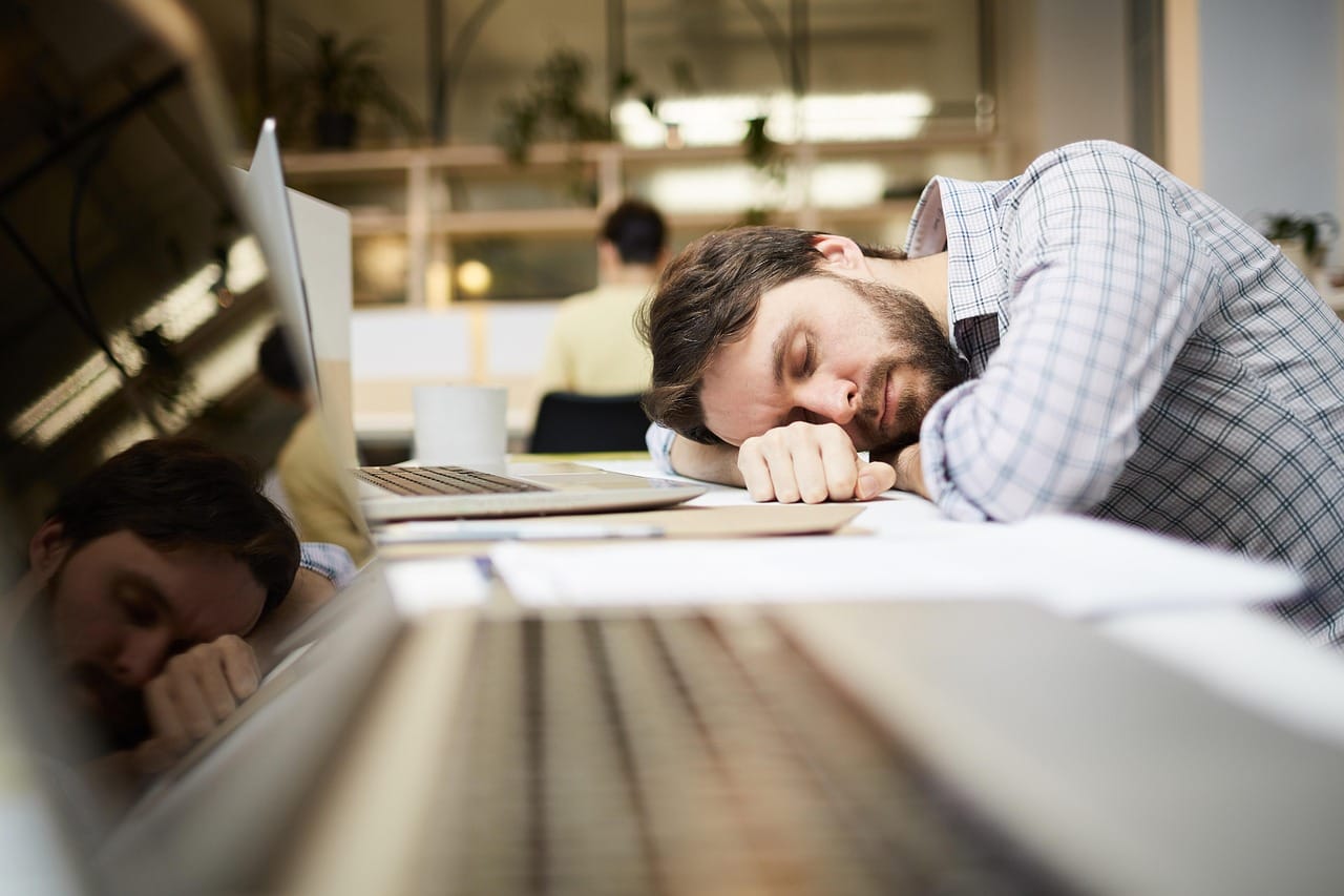 tired man falling asleep at work desk in front of computer